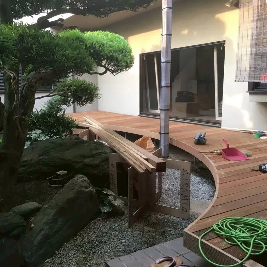 住宅の庭に沿って伸びる曲線の木製デッキ。奥に資材が置かれている